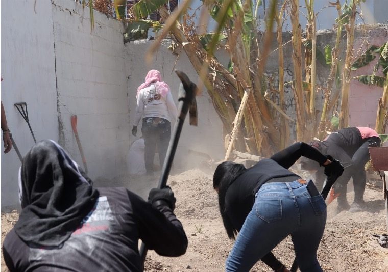 Searching mothers digging with pickaxes and shovels beside a wall