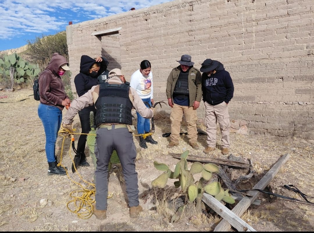 Searching families and authorities examining a site beside an adobe wall