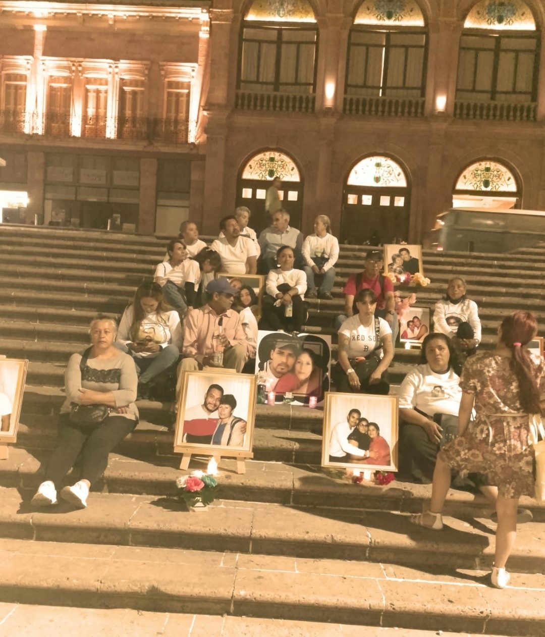 Families holding a vigil on the steps of a theatre with framed portraits of their disappeared loved ones